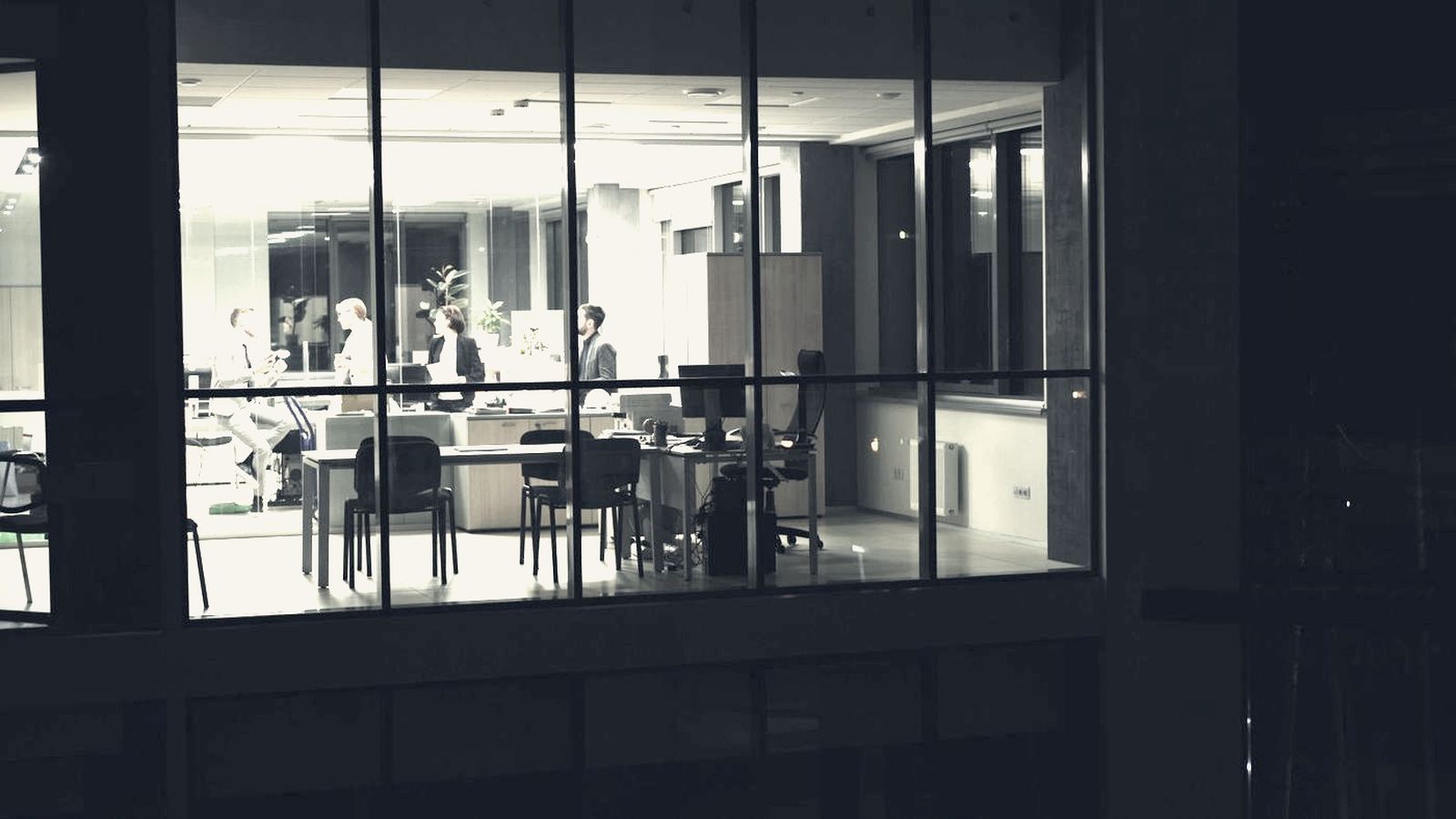 Colleagues collaborating in a glass-walled office at night