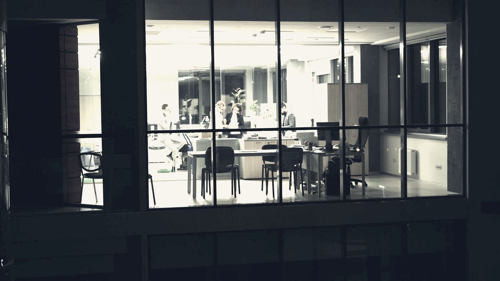 Project team meeting inside a lit office seen at night