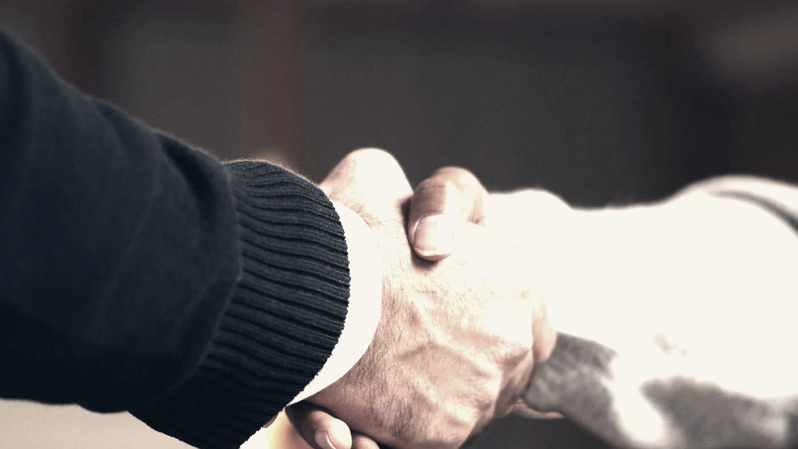 Two people shaking hands across a table in warm low light