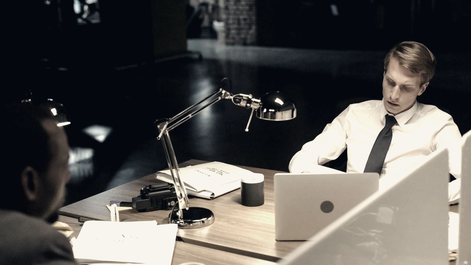 Two colleagues working late at a desk in a dimly lit office